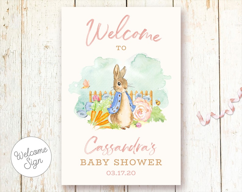 May include: Welcome to Cassandra's Baby Shower sign with a watercolor illustration of a rabbit in a blue jacket, carrots, flowers, and a fence. The date of the shower is 03.17.20.