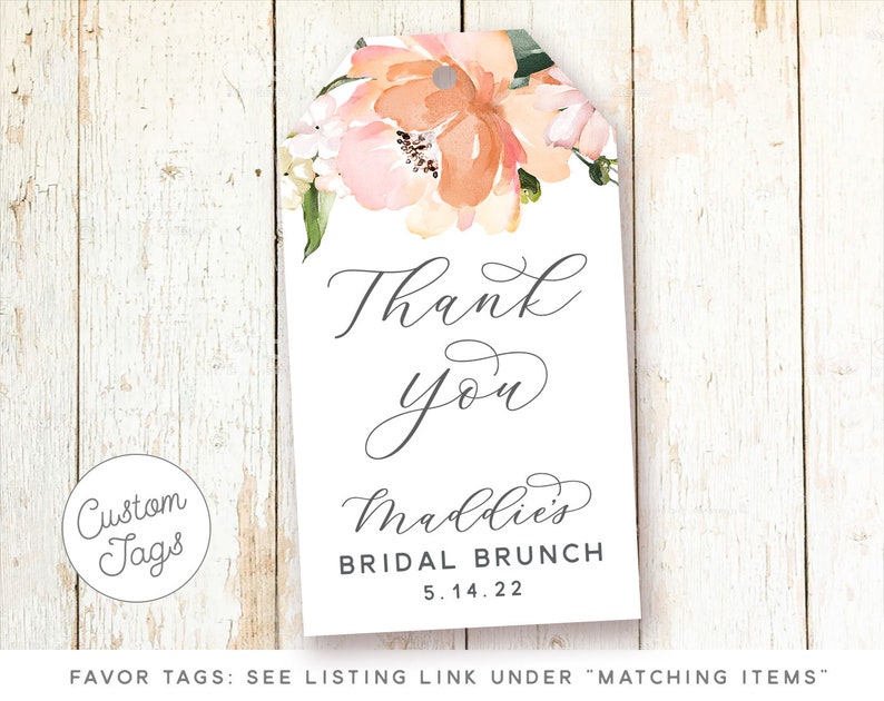 May include: A white thank you tag with a floral design in shades of pink and orange. The text "Thank you" is written in cursive script. The text "Maddie's Bridal Brunch 5.14.22" is printed below the floral design.