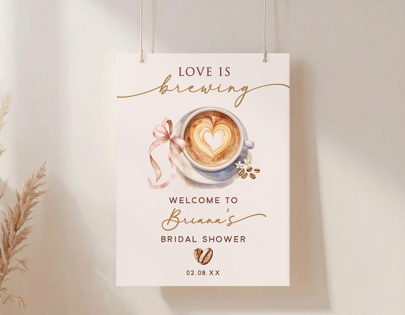 May include: A rectangular sign with the words "Love is Brewing" above a watercolor image of a coffee cup with a heart-shaped design in the foam. The sign reads "Welcome to Briana's Bridal Shower" with a date below.
