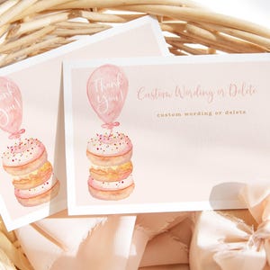 May include: Two pink cards with watercolor illustrations of donuts and balloons. One card says "Thank You!" and the other says "Custom Wording or Delete". The cards are in a woven basket with a pink ribbon.