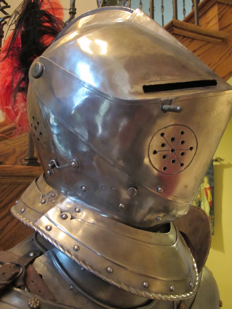 May include: A silver helmet with a plume of red and black feathers. The helmet has a visor and a decorative design on the side.