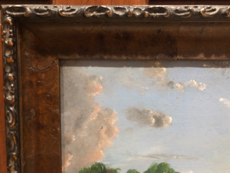 May include: A framed oil painting depicting a landscape scene with a blue sky, white clouds, and green trees in the foreground.