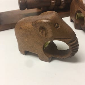 May include: A set of four wooden elephant napkin rings. The rings are made of dark brown wood and have a carved elephant design. The rings are perfect for adding a touch of whimsy to your table setting.