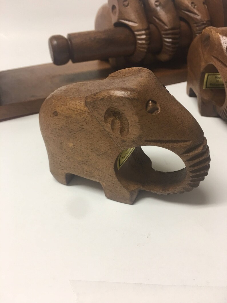 May include: A set of four wooden elephant napkin rings. The rings are made of dark brown wood and have a carved elephant design. The rings are perfect for adding a touch of whimsy to your table setting.