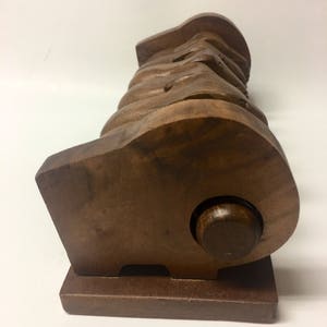 May include: A wooden sculpture of a group of hands holding each other, with a round wooden base. The sculpture is made of dark brown wood and has a smooth finish.