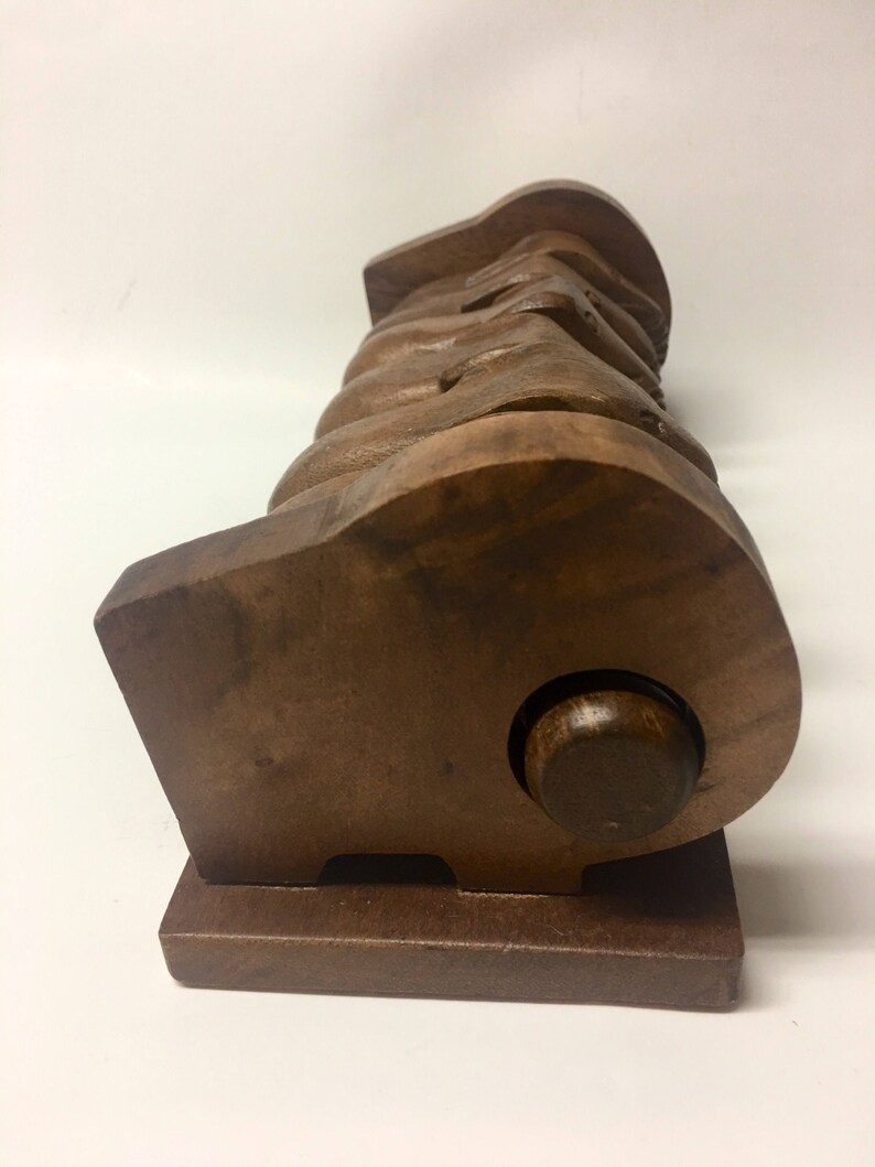 May include: A wooden sculpture of a group of hands holding each other, with a round wooden base. The sculpture is made of dark brown wood and has a smooth finish.