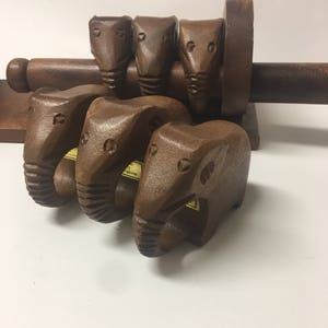 May include: Set of wooden elephant napkin rings with a wooden napkin holder. The napkin rings are brown and have a carved elephant design. The napkin holder is also brown and has a cylindrical shape.
