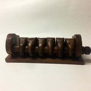 May include: A wooden puzzle with six carved elephant heads that slide along a track. The puzzle is brown and has a simple design.