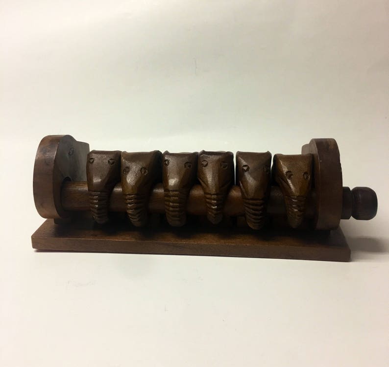 May include: A wooden puzzle with six carved elephant heads that slide along a track. The puzzle is brown and has a simple design.