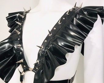 May include: A black latex harness with a ruffled neckline and silver spikes. The harness has a large silver ring in the front and adjustable straps in the back.