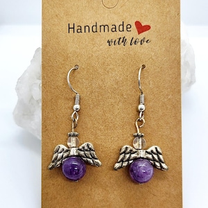 Puede incluir: Un par de pendientes de alas de &aacute;ngel hechos a mano con cuentas de piedras preciosas moradas. Los pendientes tienen alas y ganchos de metal plateado. La tarjeta dice "Handmade with love."