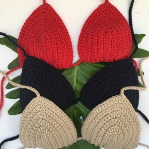 Peut inclure: Trois hauts de bikini en crochet de couleur rouge, noir et beige. Les hauts sont superpos&eacute;s et dispos&eacute;s sur une feuille verte.