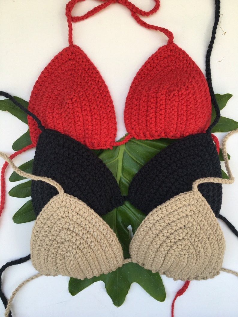 Peut inclure: Trois hauts de bikini en crochet de couleur rouge, noir et beige. Les hauts sont superpos&eacute;s et dispos&eacute;s sur une feuille verte.