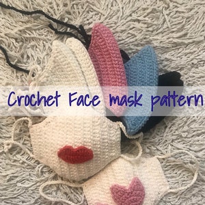 Puede incluir: Patrón de máscara facial de crochet con una máscara blanca con un diseño de labios rojos, una máscara rosa con un diseño de corazón rosa, una máscara azul y una máscara negra.