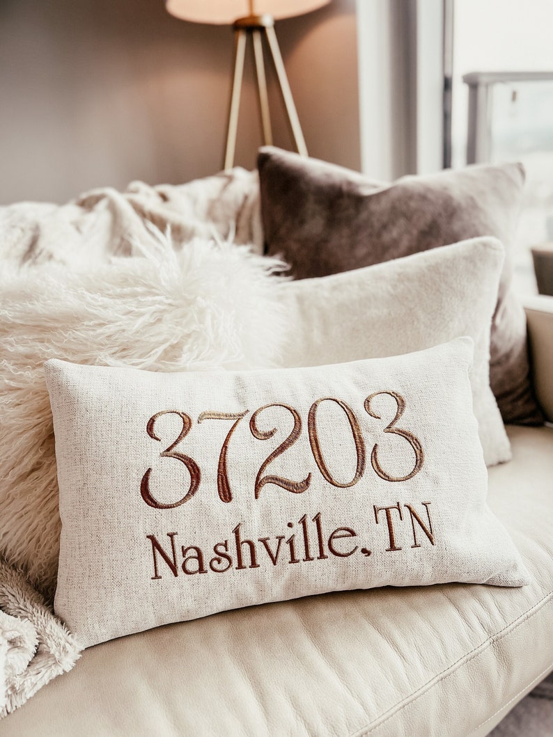 May include: A white linen cushion with brown embroidery featuring the text "37203 Nashville, TN".