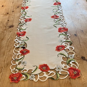 Pode incluir: Caminho de mesa bege com bordados de papoilas vermelhas, margaridas brancas e folhas verdes. As bordas apresentam um design ondulado. Perfeito para uma mesa de jantar ou aparador.