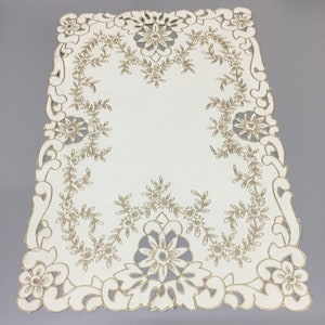 May include: White table runner with a gold embroidered floral design. The design features intricate details and a delicate lace-like border.