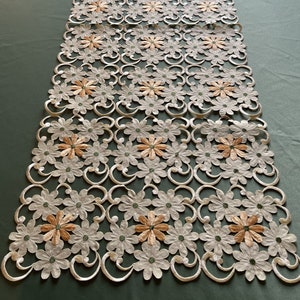 May include: White crocheted table runner with a delicate floral pattern. The runner features a repeating design of small, peach-colored flowers.