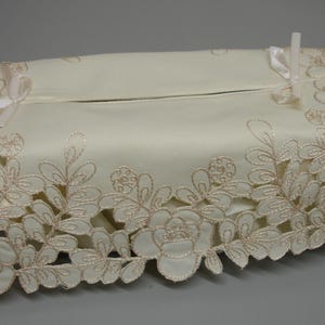 Puede incluir: Funda de caja de pañuelos de color marfil con un ribete de encaje floral. La funda rectangular tiene una ranura para dispensar pañuelos. Delicados bordados florales de color melocotón adornan los bordes, y pequeños lazos añaden un toque decorativo.