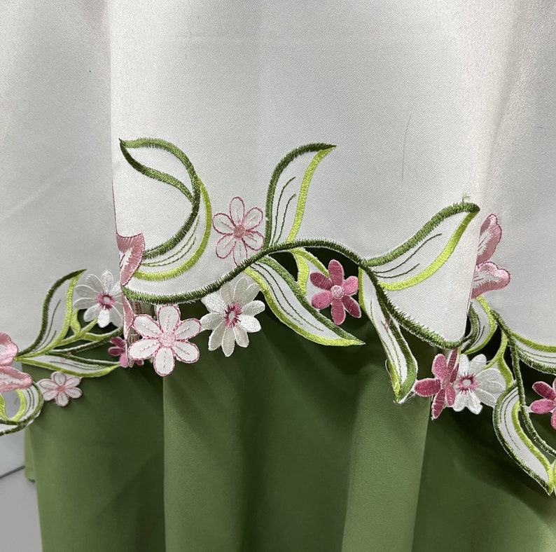 May include: White tablecloth with a green and pink floral embroidered border. The embroidery features delicate leaves and flowers.