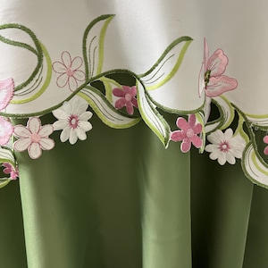 May include: White tablecloth with green and pink embroidered floral design. The tablecloth has a green scalloped edge.