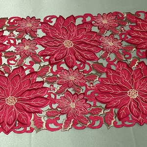 May include: Red embroidered table runner with a poinsettia design. The runner features a cut-out pattern and is perfect for adding a festive touch to your holiday table.