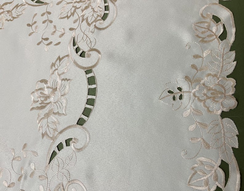 May include: White table runner with a delicate floral embroidery design in a cream color. The embroidery features intricate floral patterns, including roses and leaves, along the edges of the runner.