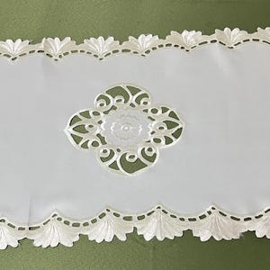Può includere: Tovaglia da tavolo ovale bianca con un delicato disegno in pizzo con motivi floreali. La tovaglia ha un bordo a festoni ed è realizzata in un tessuto bianco morbido.