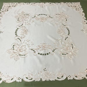 May include: White embroidered tablecloth with a floral design. The tablecloth has a delicate lace pattern around the edges and features a central floral motif.