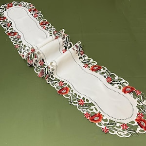 Può includere: Runner da tavolo bianco con un motivo floreale. Il runner presenta un bordo smerlato con fiori di papavero rossi e foglie verdi. Il centro è di colore bianco pieno con un bordo a pois.