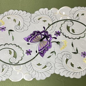 May include: White table runner with a delicate embroidered design featuring purple butterflies and floral accents.