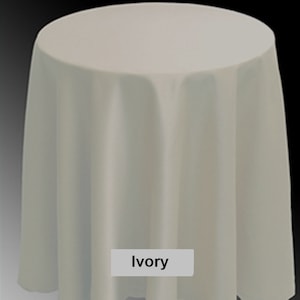 May include: Ivory-colored round tablecloth. The fabric drapes over a round table, creating soft folds. The tablecloth is a solid, neutral color, suitable for various event themes. The word "Ivory" is displayed in a white rectangle.