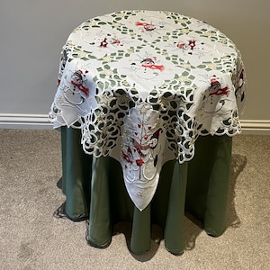 May include: White table cloth with a green background. The tablecloth has a lace design with embroidered snowmen and robins.