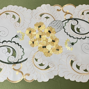 Peut inclure: Un chemin de table blanc avec un motif floral délicat. Le chemin de table présente des broderies dorées et vertes de fleurs et de feuilles stylisées.
