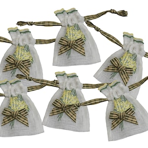 May include: Six white sachets with embroidered yellow floral designs and brown plaid bows. Each sachet has a green and brown plaid ribbon tie. The sachets are likely filled with potpourri or herbs.