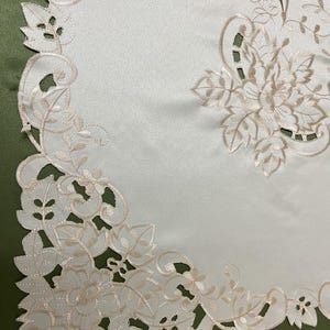 May include: White table runner with a delicate floral embroidery design in a cream color. The embroidery features intricate leaves and flowers, creating a classic and elegant look.