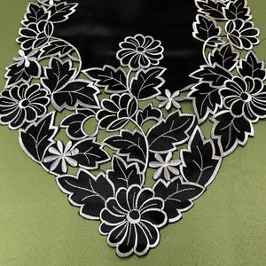 May include: Black table runner with a silver floral design. The runner features a repeating pattern of leaves and flowers.