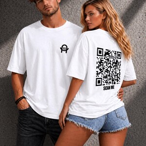 Könnte beinhalten: Weiße T-Shirts mit schwarzen Grafiken. Ein Shirt hat ein kleines Logo auf der Vorderseite, das andere einen QR-Code auf der Rückseite mit dem Text "SCAN ME". Die Shirts werden von zwei Personen getragen.