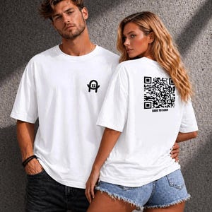 Könnte beinhalten: Ein weißes T-Shirt mit kurzen Ärmeln, das auf der Brust ein kleines schwarzes Logo mit der Zahl 13 und auf der Rückseite einen großen schwarzen QR-Code mit dem Text DARE TO SCAN in schwarzen Großbuchstaben unter dem Code zeigt.