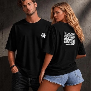 Könnte beinhalten: Ein schwarzes kurzärmeliges T-Shirt mit einem kleinen weißen Logo auf der Brust und einer großen weißen QR-Code-Grafik auf der Rückseite, unter der der Text DARE TO SCAN steht. Das T-Shirt hat einen Rundhalsausschnitt und eine lockere Passform.
