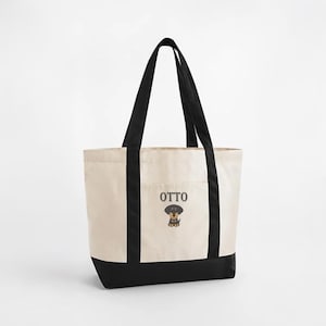 May include: Cream-colored tote bag with black accents and handles. The bag features the name "OTTO" above a cartoon dachshund illustration. The bottom of the bag and the vertical sides are black.
