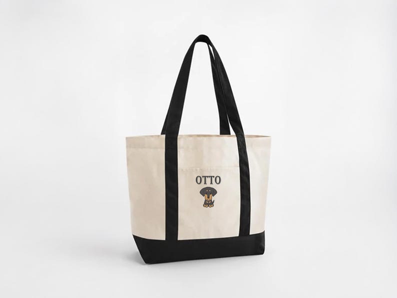 May include: Cream-colored tote bag with black accents and handles. The bag features the name "OTTO" above a cartoon dachshund illustration. The bottom of the bag and the vertical sides are black.