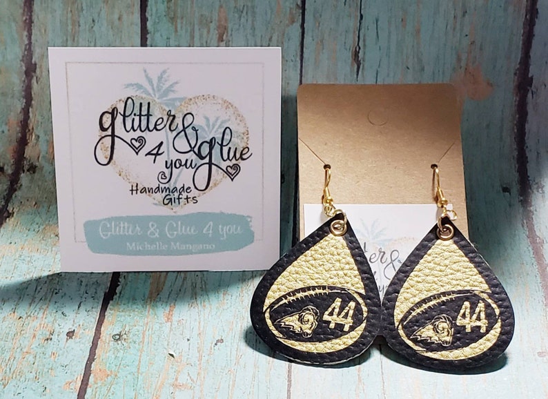Puede incluir: Un par de pendientes de cuero en forma de l&aacute;grima de color negro y dorado con un dise&ntilde;o de f&uacute;tbol y el n&uacute;mero 44. Los pendientes tienen ganchos dorados.