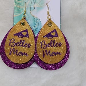May include: A pair of gold and purple glitter earrings with a purple megaphone and the text "Belles Mom" on each earring.