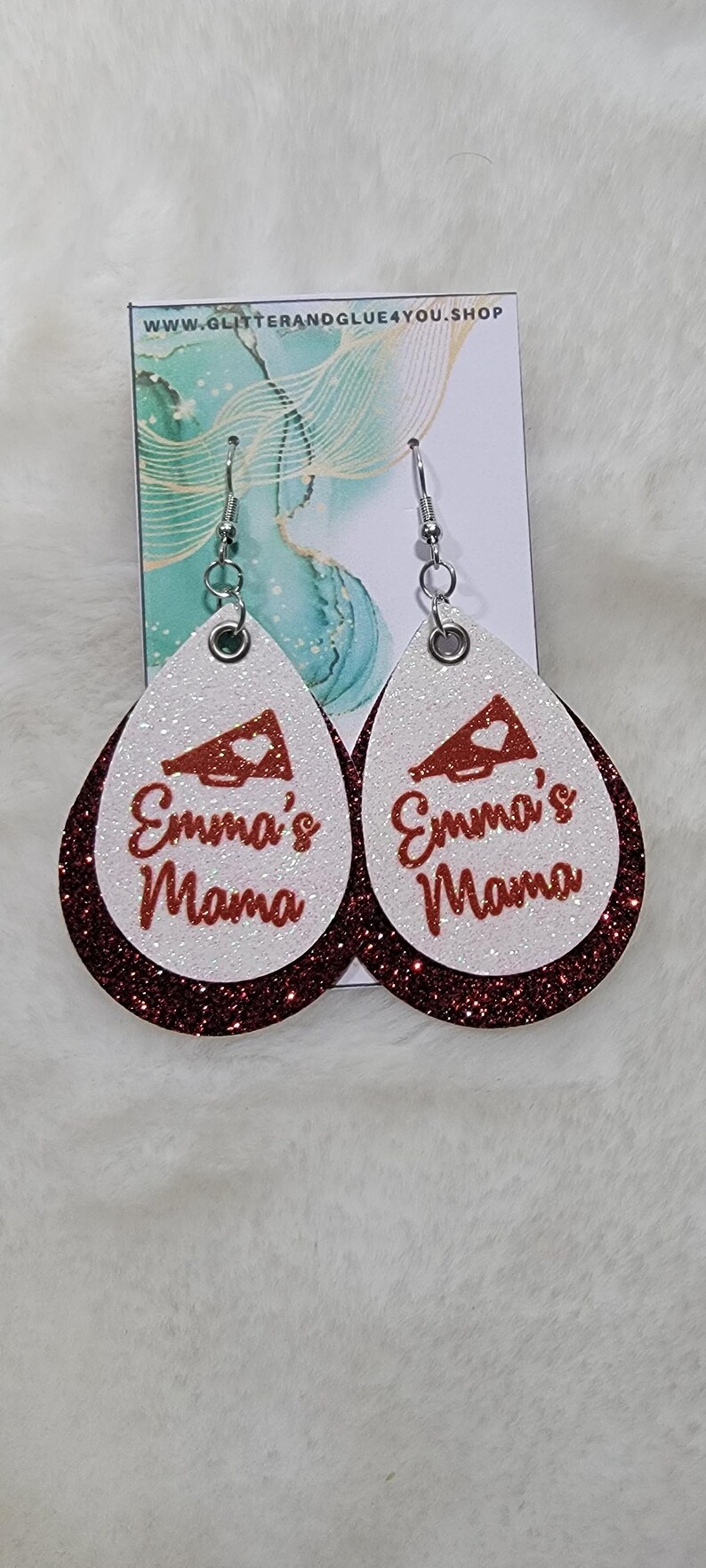 May include: A pair of red and white glitter earrings with a white megaphone and the text "Emma's Mama" in red glitter.