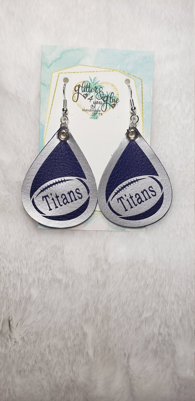 Puede incluir: Pendientes de cuero en forma de l&aacute;grima plateados con un dise&ntilde;o de f&uacute;tbol azul y la palabra "Titans" impresa en cada pendiente.