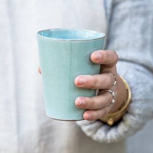 A handmade pottery Turquoise tumbler in a hand.