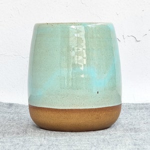 May include: A light blue ceramic mug with a brown rim. The mug is sitting on a light gray fabric surface.