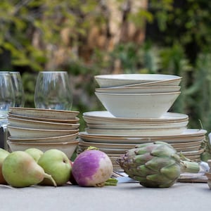 May include: A table setting with white ceramic bowls and plates, wine glasses, and fresh produce, including artichokes, pears, and turnips.