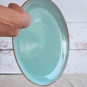 Może przedstawiać: Jasnoniebieski talerz ceramiczny z brązową obw&oacute;dką. Talerz jest okrągły i ma gładką, błyszczącą powierzchnię.